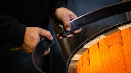 Tonnelier plaçant un cercle métallique sur un fût chauffé à la Tonnellerie Remond.